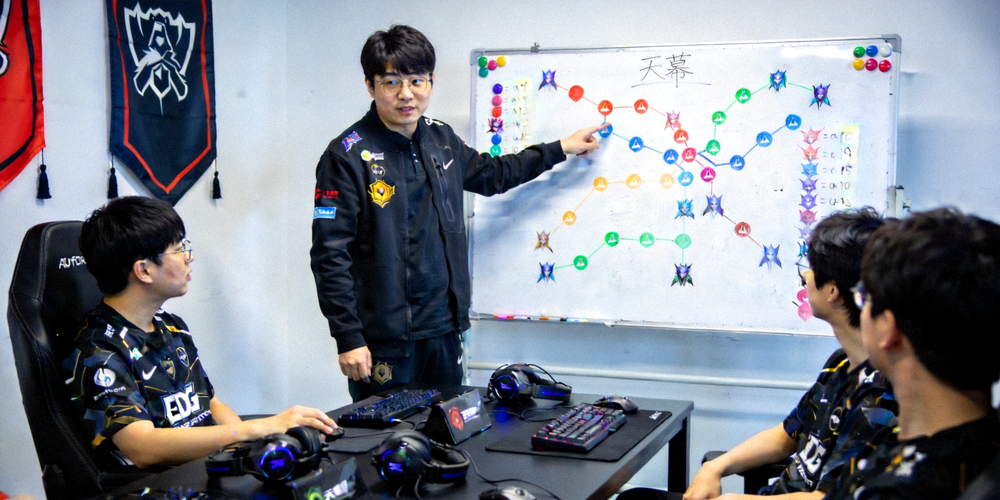 天幕战队教练在休息室与选手进行战术部署，白板上画满战术路线与英雄选择